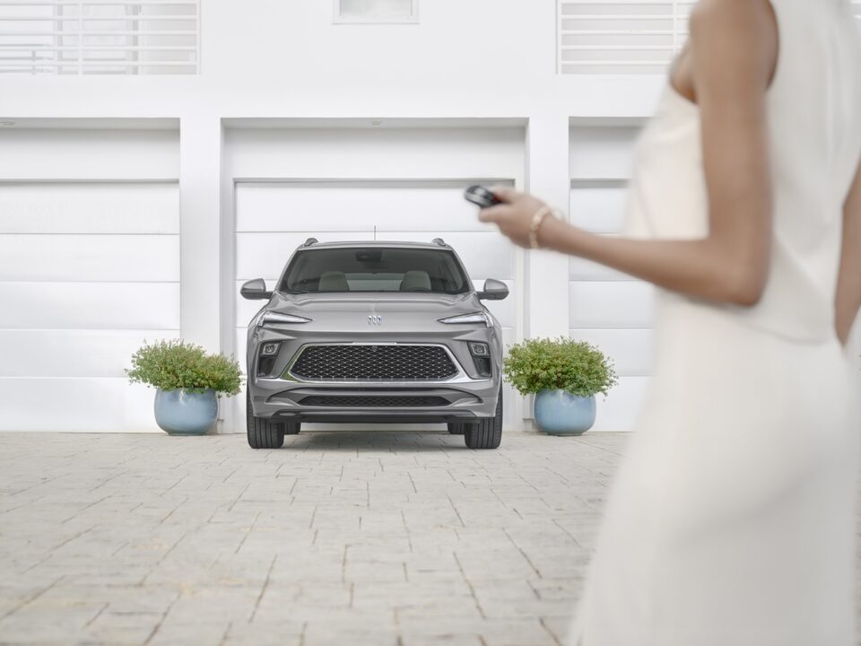 Captivating front-view of the 2024 Encore GX Avenir parked outside a building as a woman passes by.