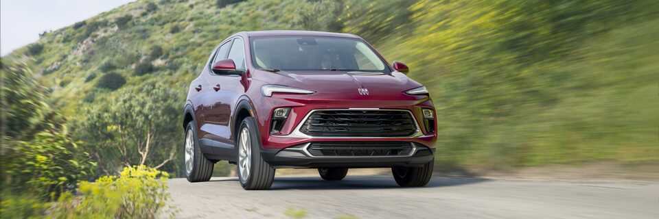 Red-colored 2024 Encore GX driving on a hillside road.