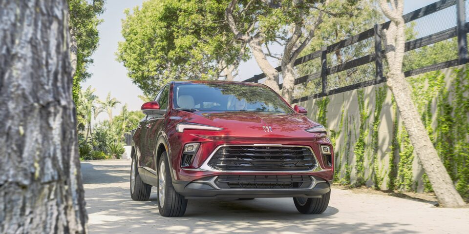 Red-colored 2024 Encore GX driving next to a fence.