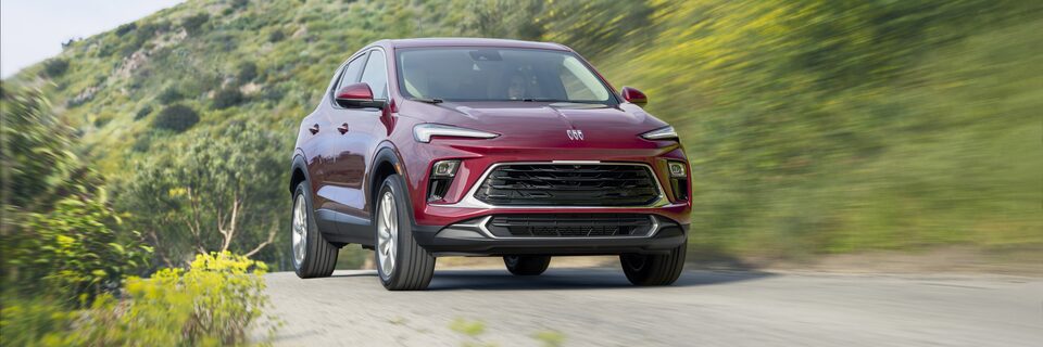 The 2024 Buick Encore GX driving on a tree-lined road.