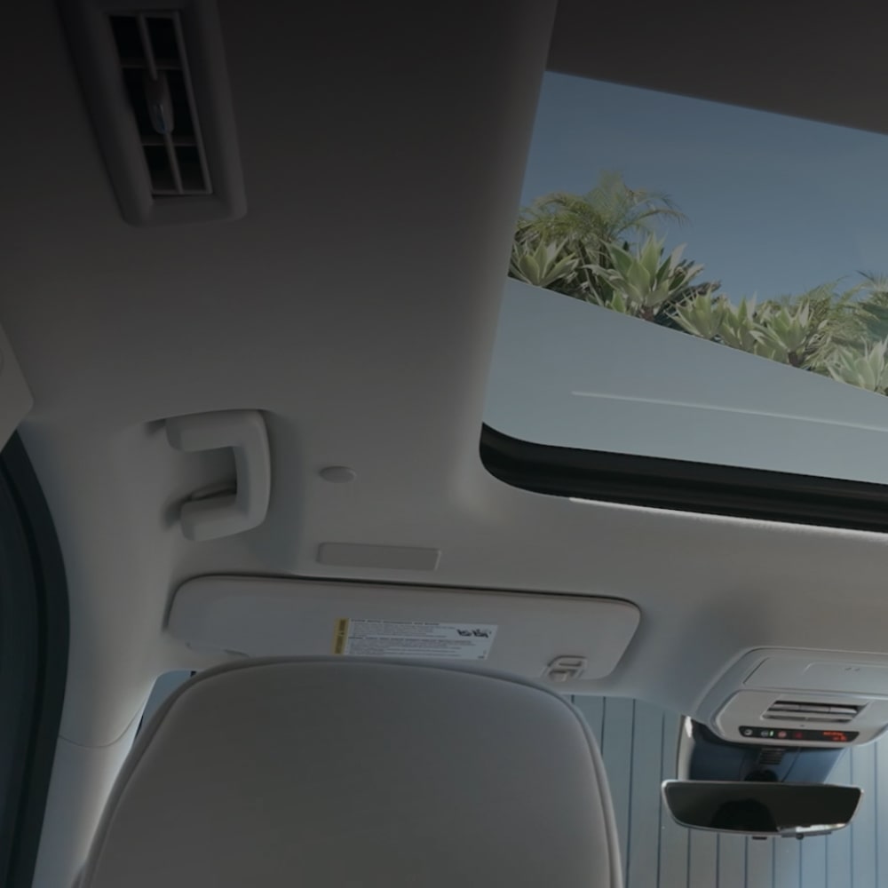 Une vue intérieure regardant vers le toit panoramique de la Buick Enclave 2027, révélant un ciel bleu et des palmiers verts.