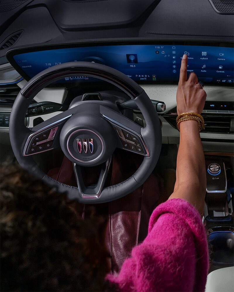 La main du conducteur interagit avec l’immense écran numérique courbé de l’intérieur d’une Buick Enclave 2027.