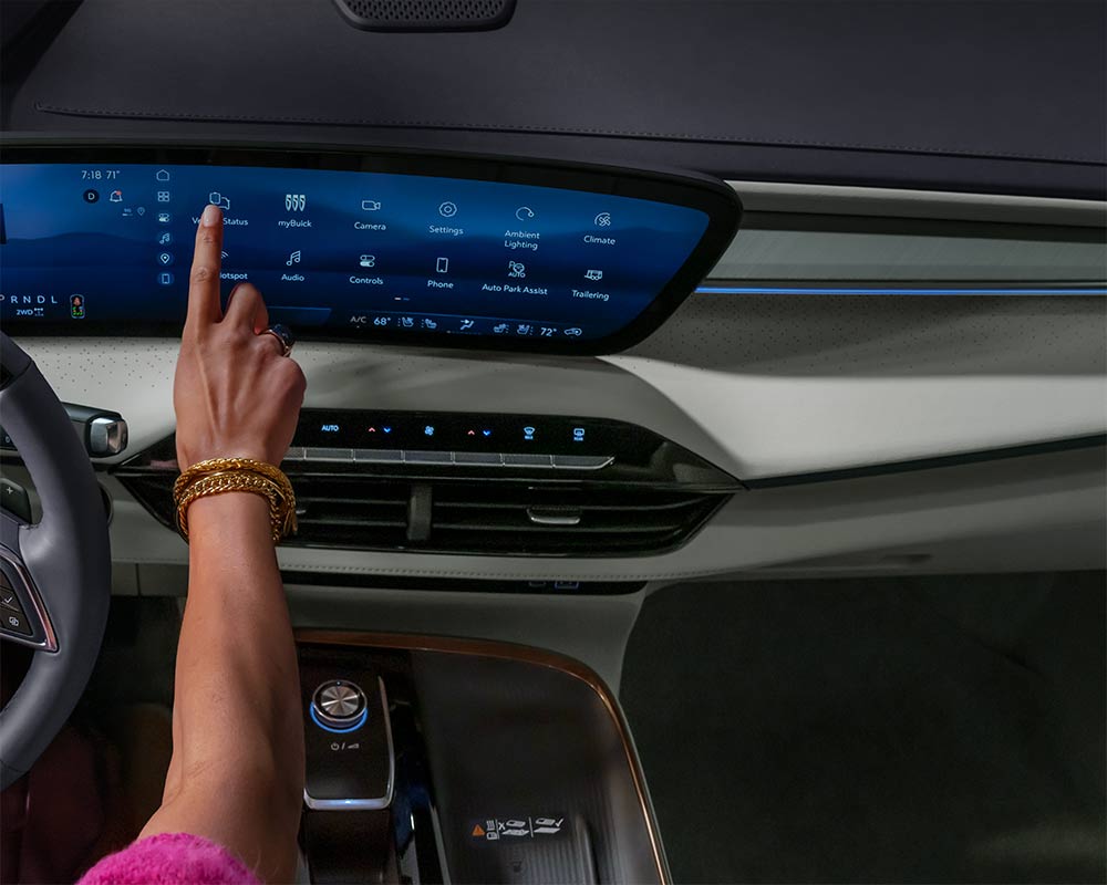 Une main avec des bracelets dorés touchant un grand écran tactile à l’intérieur d’une Buick Enclave Avenir 2027.