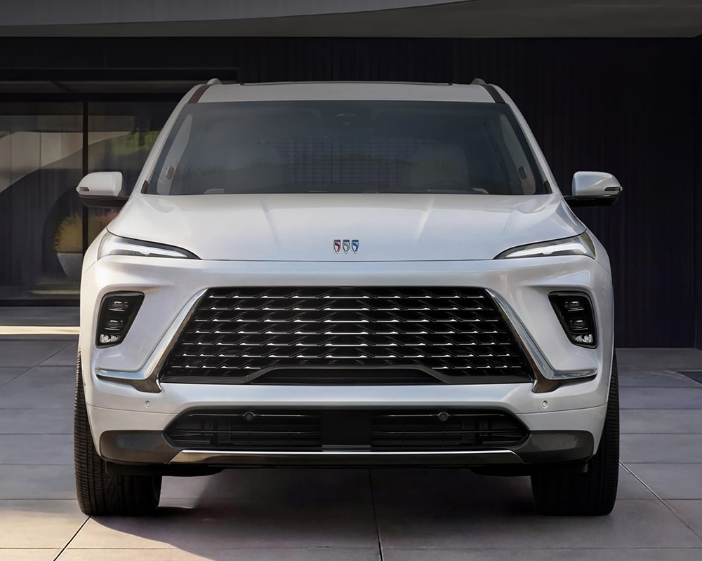 Vue de face d’un VUS blanc Buick Enclave Avenir 2027 stationné devant un bâtiment moderne.