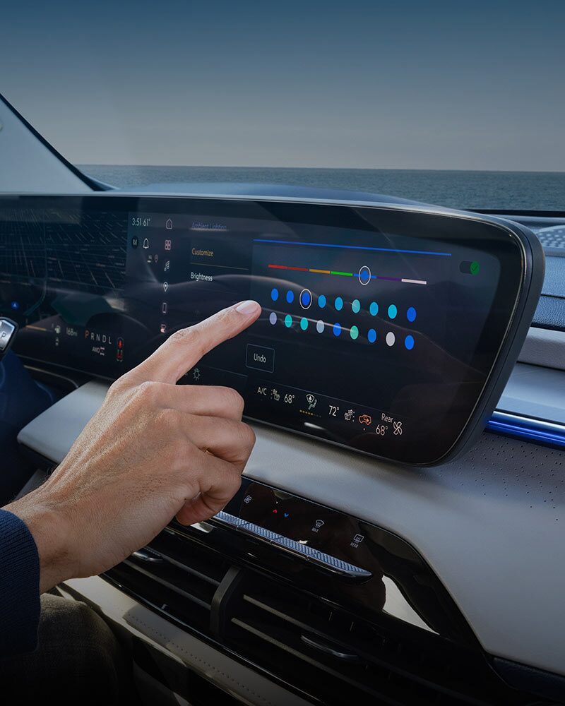 Une main interagissant avec l’écran tactile d’infodivertissement d’une Buick Enclave 2027 pour ajuster les réglages d’éclairage ambiant.