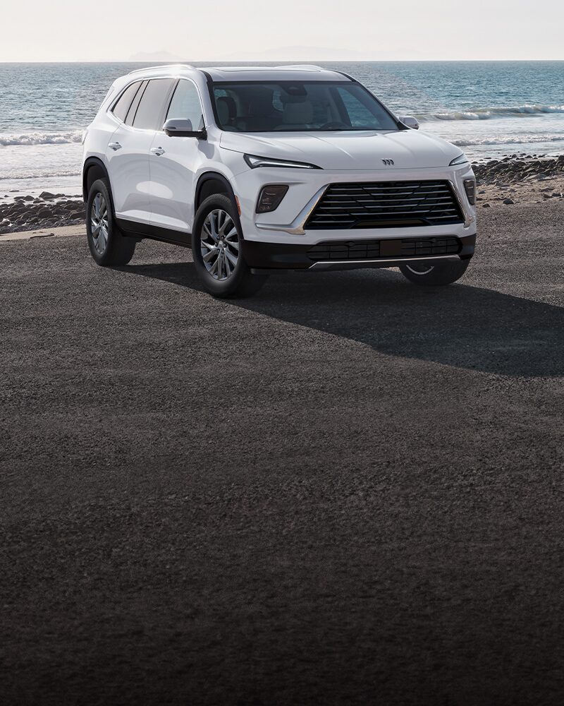 Un VUS blanc Buick Enclave Preferred 2027 stationné sur une route de plage avec l’océan en arrière-plan.
