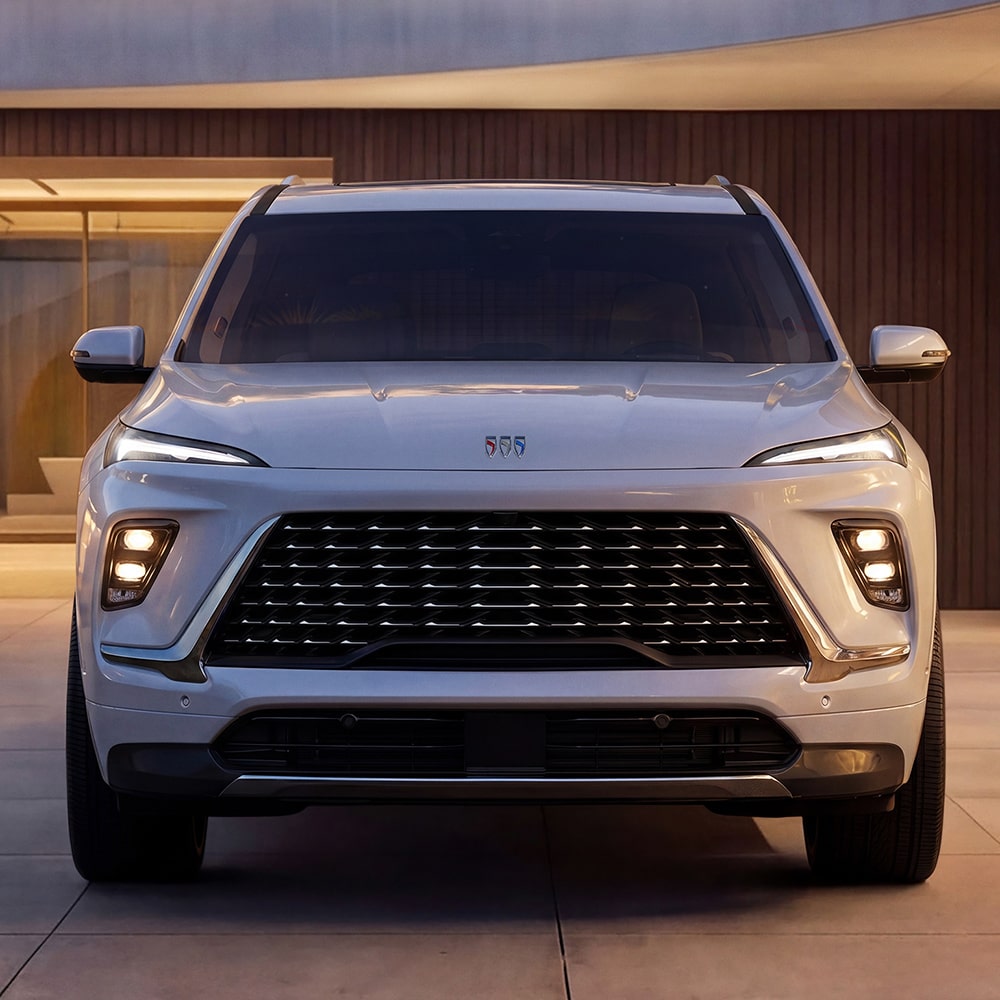 The Front View of a White 2027 Buick Enclave Avenir SUV Parked in Front of a Modern Building.