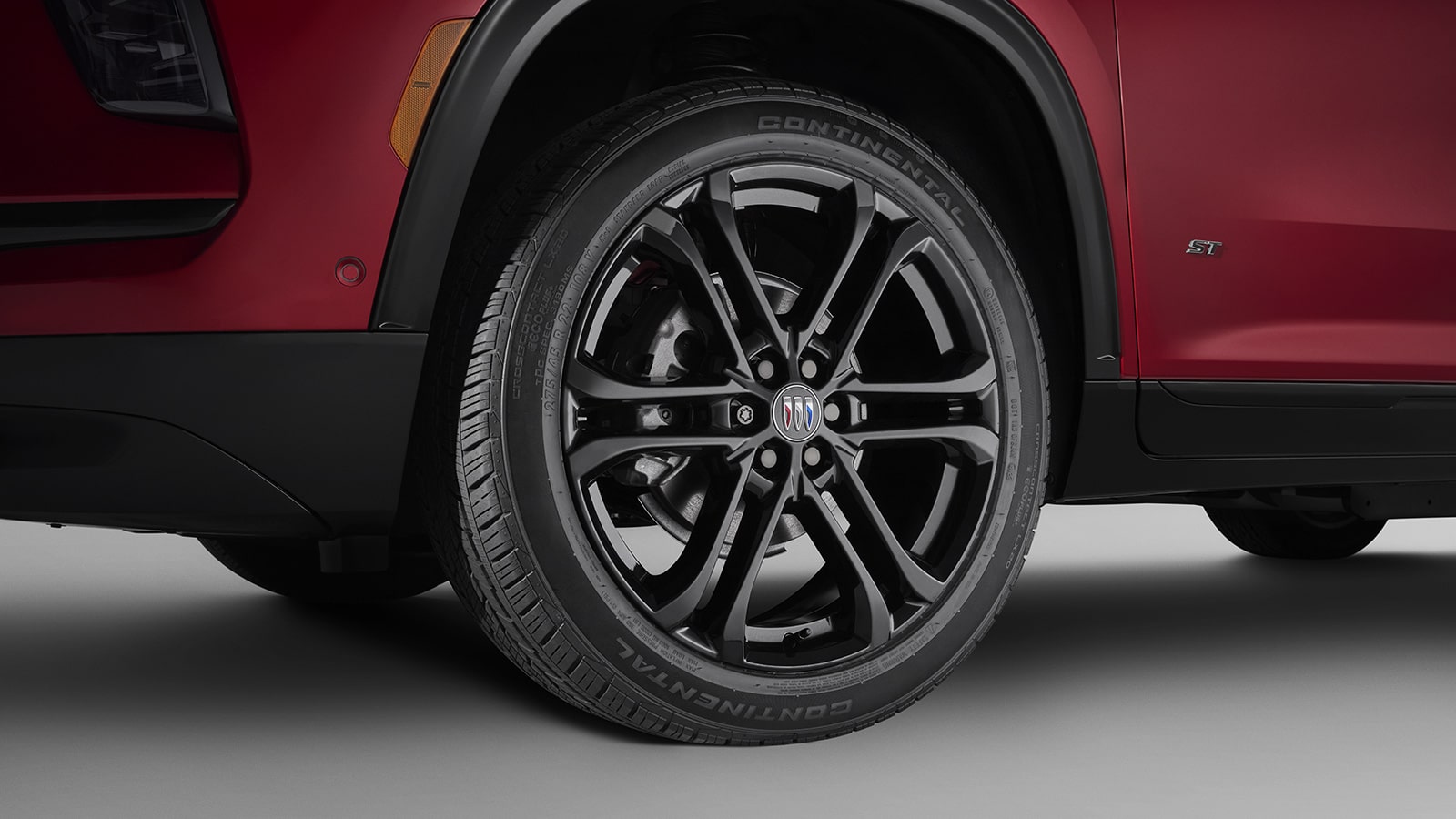 A Close-up of a Black Multi Spoke Wheel with a Buick Logo on a Red 2027 Buick Enclave Avenir SUV.