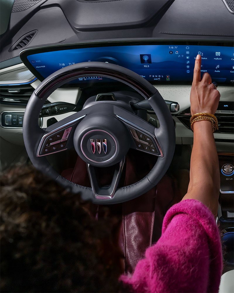 A Driver's Hand Interacts with the Expansive Curved Digital Display in a Modern 2027 Buick Enclave Avenir Interior, Featuring the Buick Logo on the Steering Wheel.