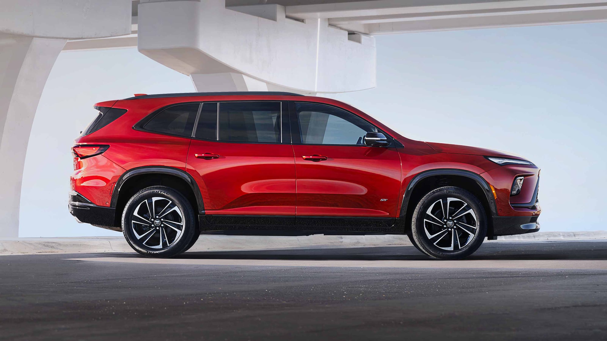 Un VUS Buick Enclave rouge 2027 stationné de profil sous une arche architecturale moderne