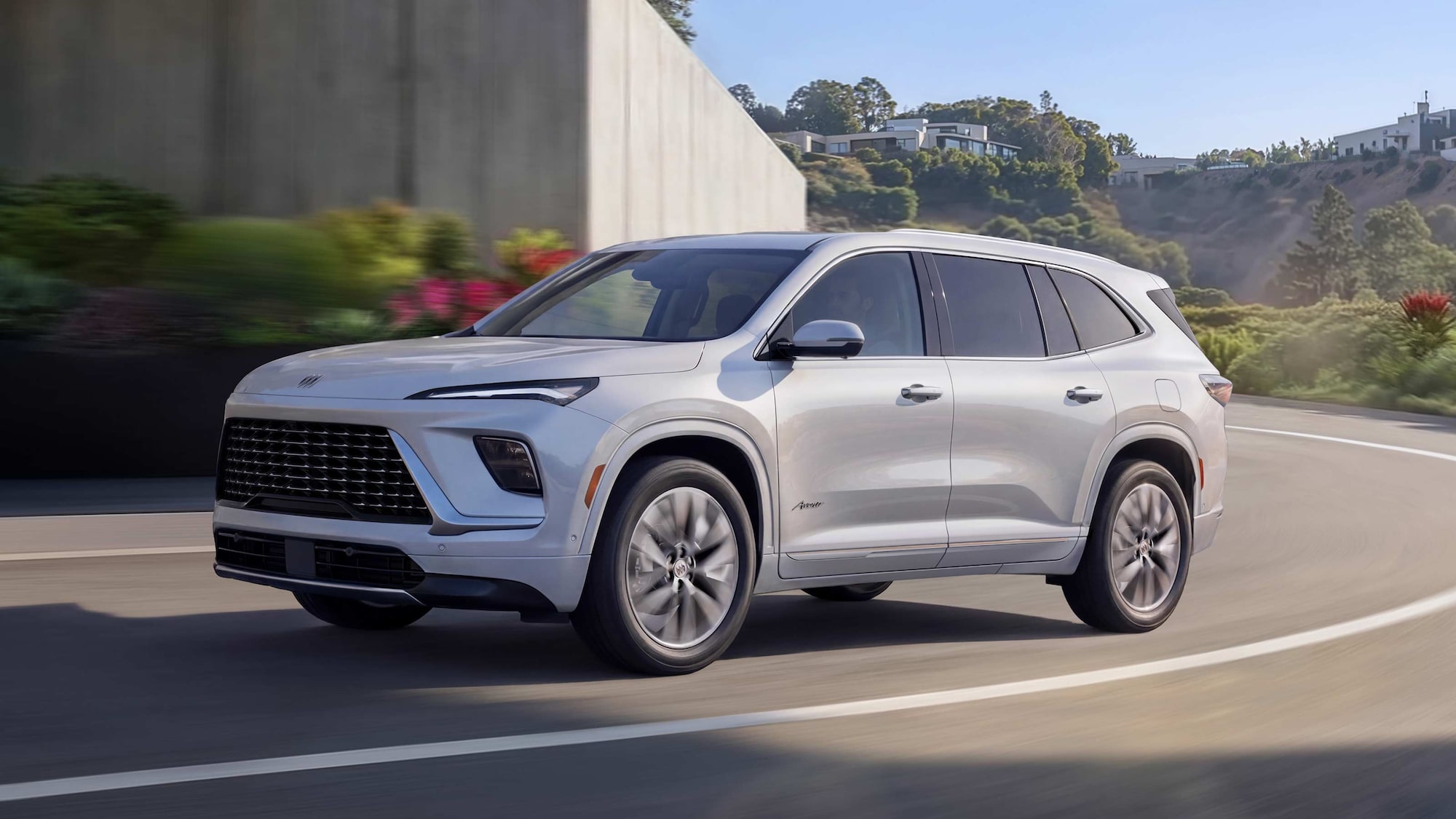 Un VUS blanc Buick Enclave Avenir 2027 roulant sur une route en courbe.