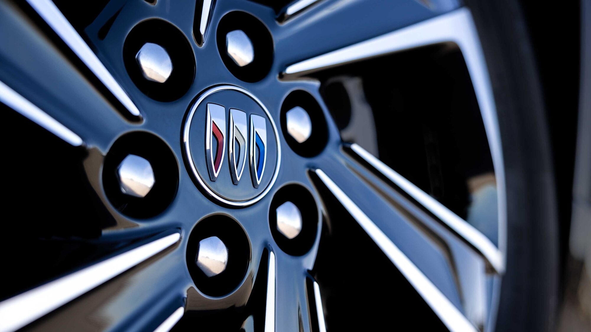 Vue rapprochée d’une roue de voiture noire brillante avec des rayons argentés et le logo Buick 2027 au centre