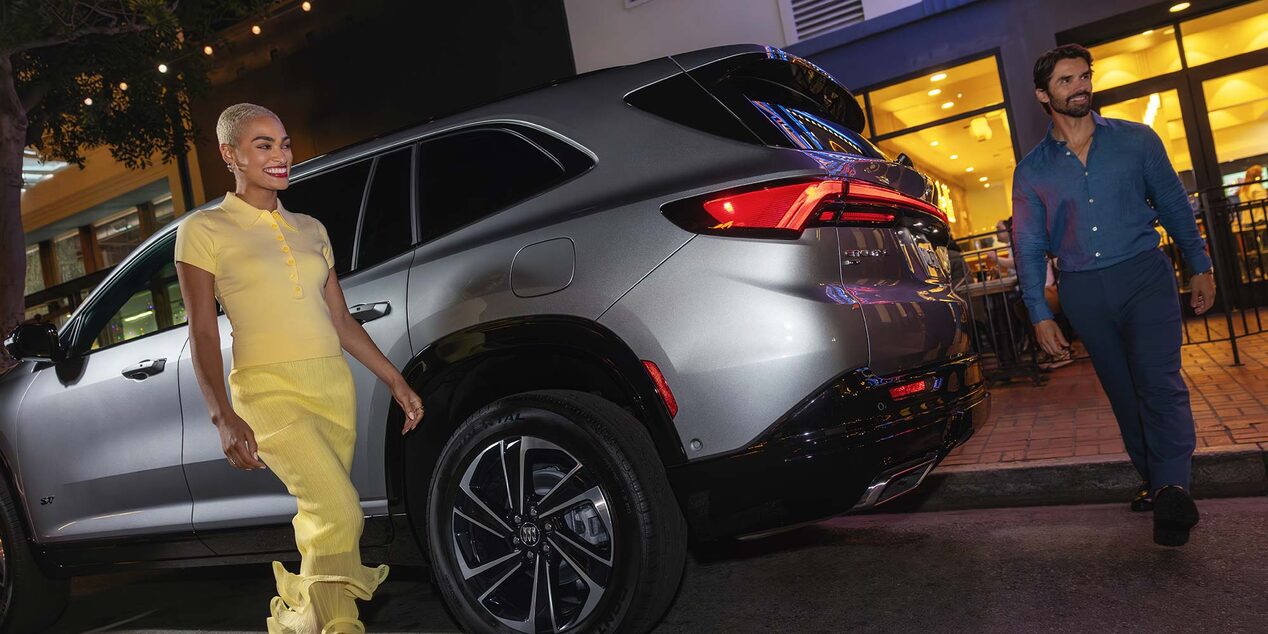 Deux personnes sortant d’une Buick Enclave 2027 garées devant un restaurant.