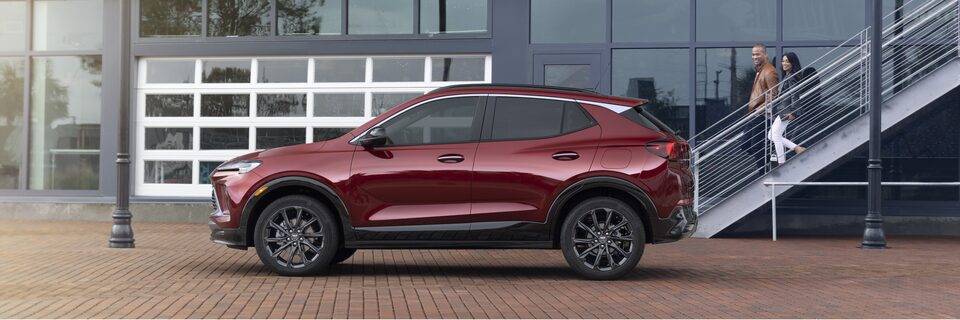 Red-colored 2024 Encore GX ST parked outside a building.