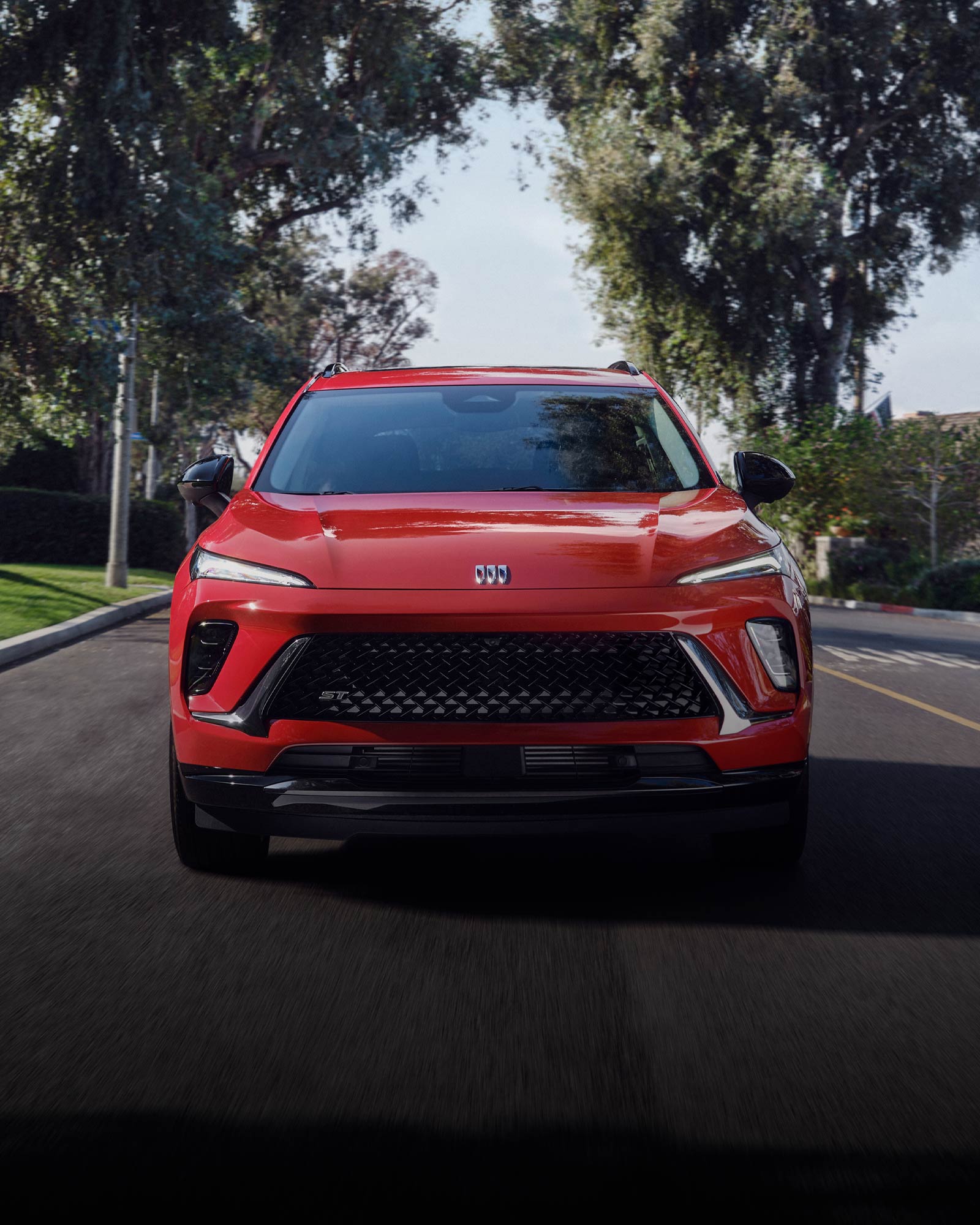Front View of the 2026 Buick Envision ST Sporty Compact SUV Driving Down a Black Top Road.