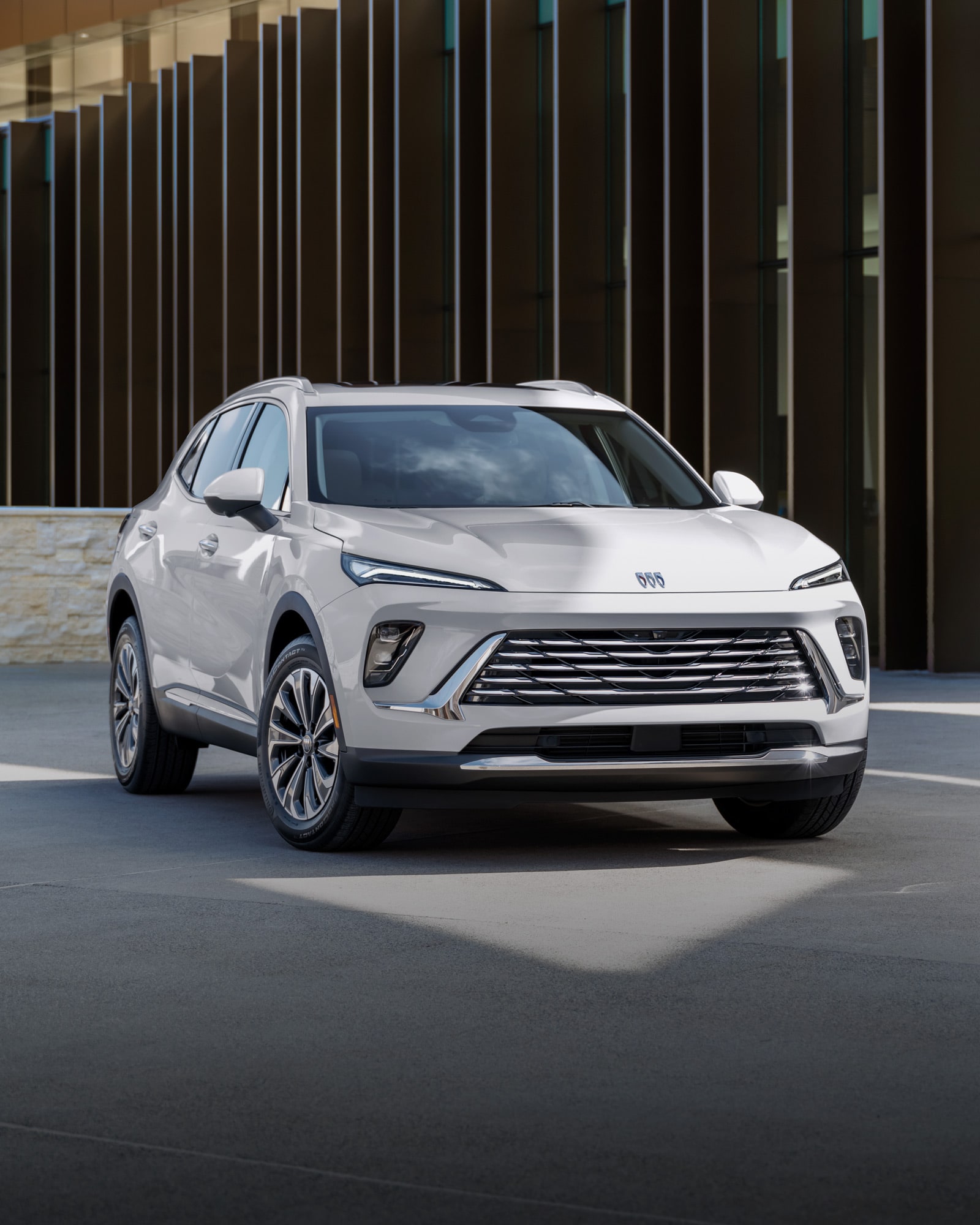 Front Three-Quarters View of the 2026 Buick Envision Preferred 5 Passenger SUV Driving Down a Tree Lined Road.