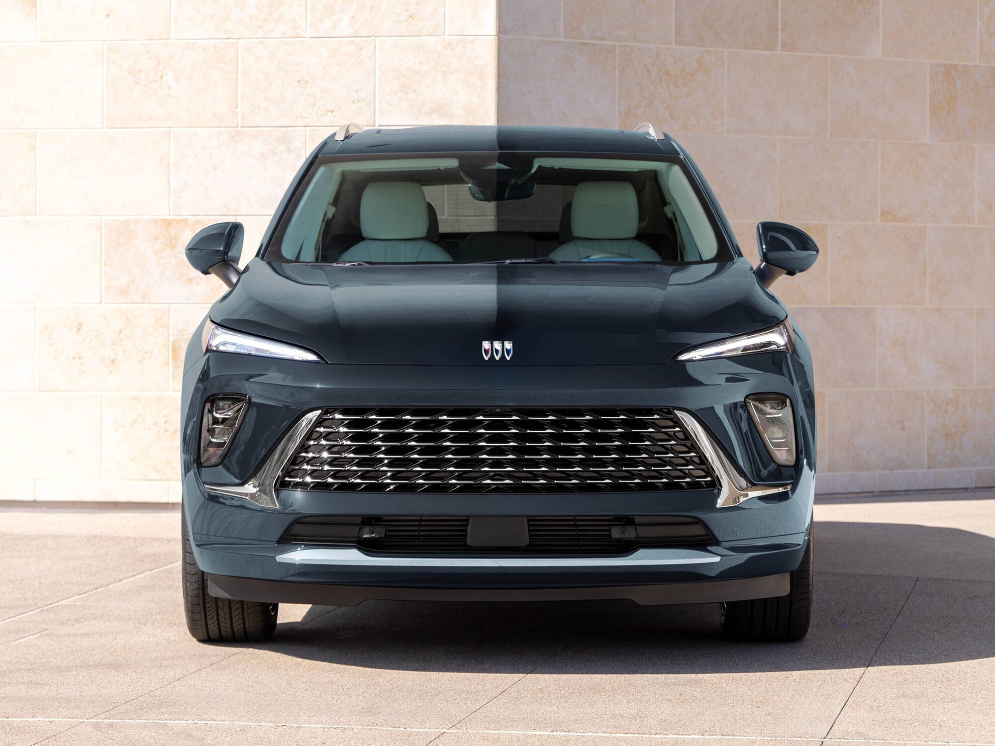 A Front View of the Dark Blue 2025 Buick Envision SUV Parked Against a Modern Stone Wall