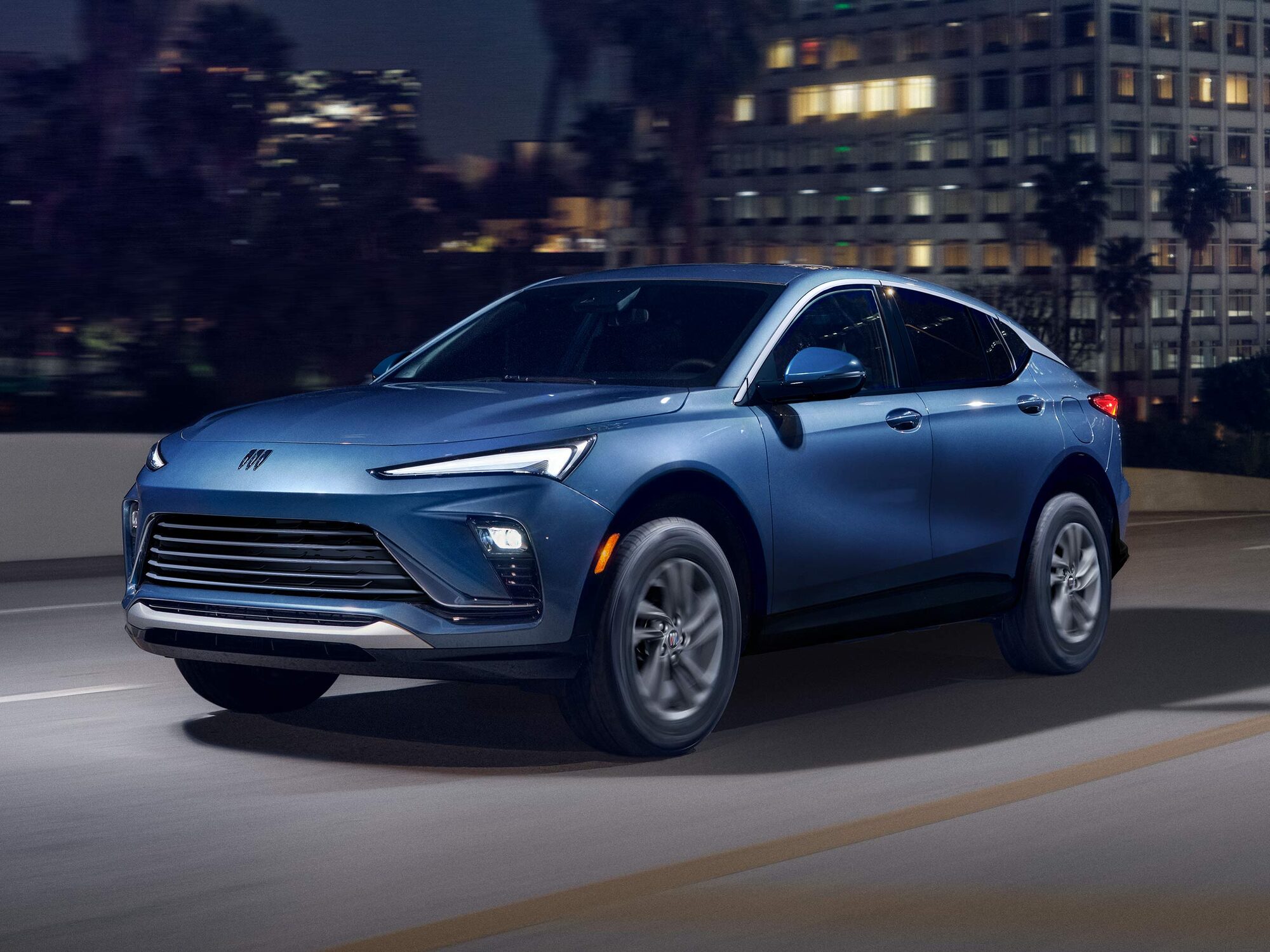  A Blue Buick Envista ST Driving on a City Street at Night with Blurry City Lights in the Background 