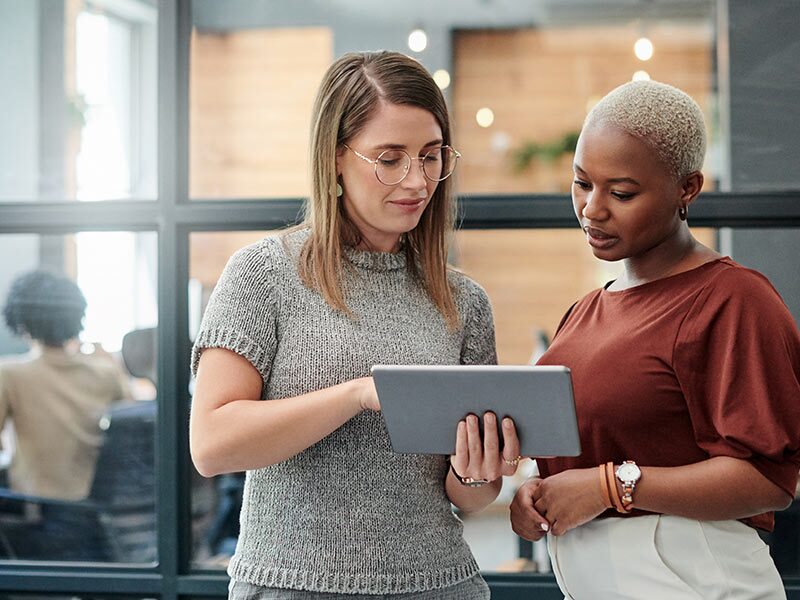 Two People Looking at a Tablet Together with a Conference Room in the Background
