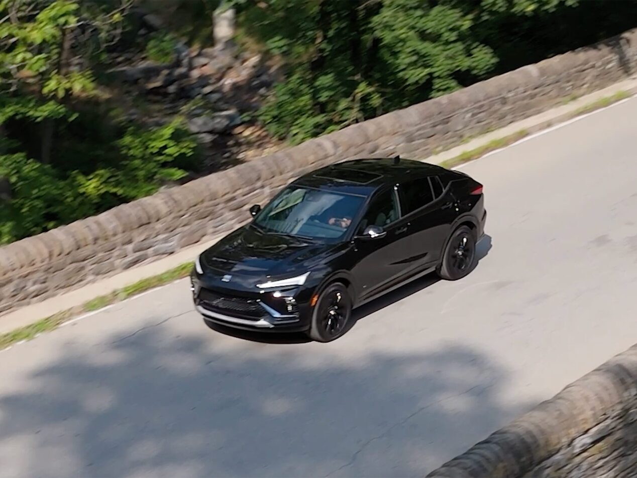 A Black Buick Envista Sport Touring Driving on a Stone Bridge Road with Green Trees