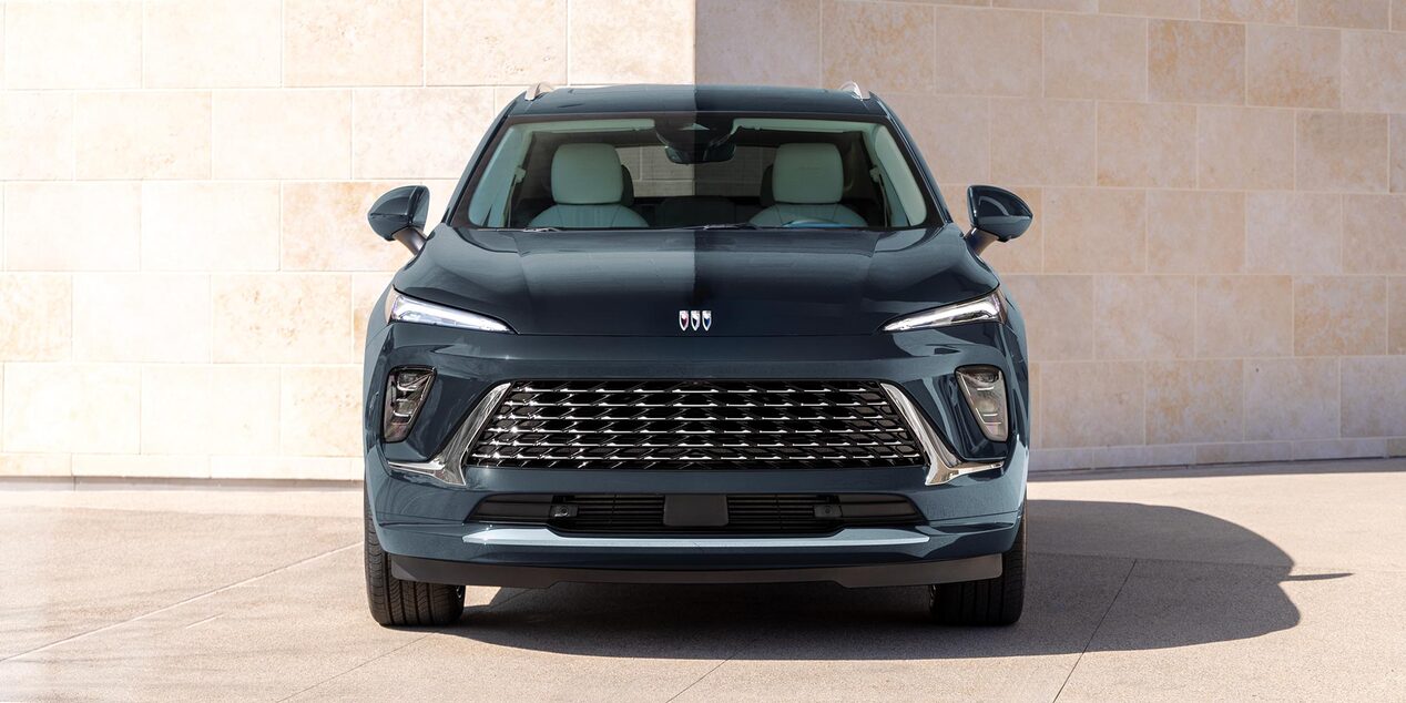 A Front View of a Dark Gray Buick SUV with a Distinctive Grille Parked by a Stone Wall