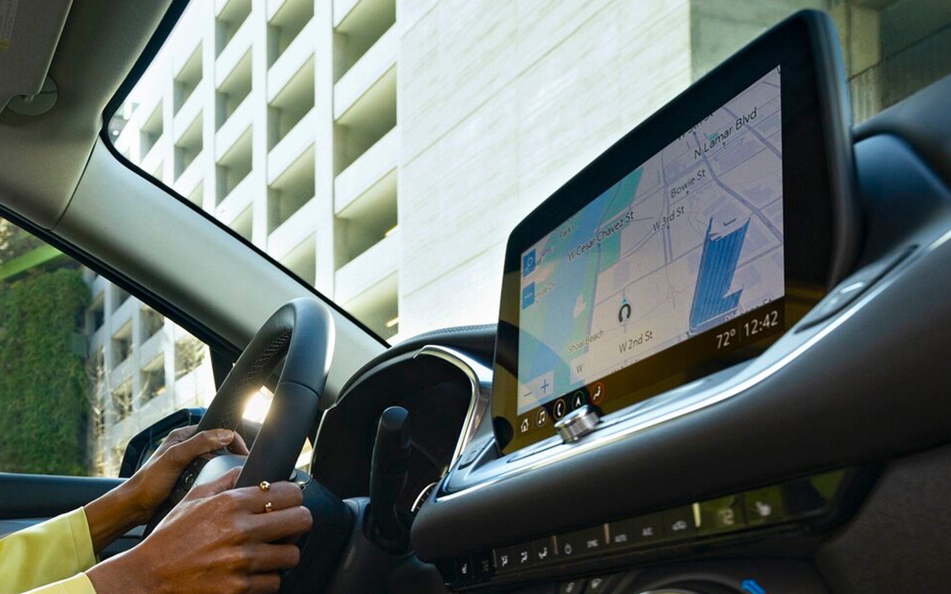 Interior View of the Buick Infotainment System Displaying the Navigation App as a Woman Drives Through the City