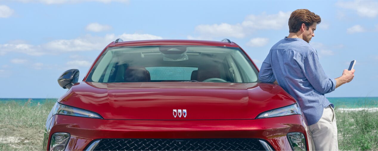 A Man Leaning on the Hood of His Buick Vehicle Using His Smartphone