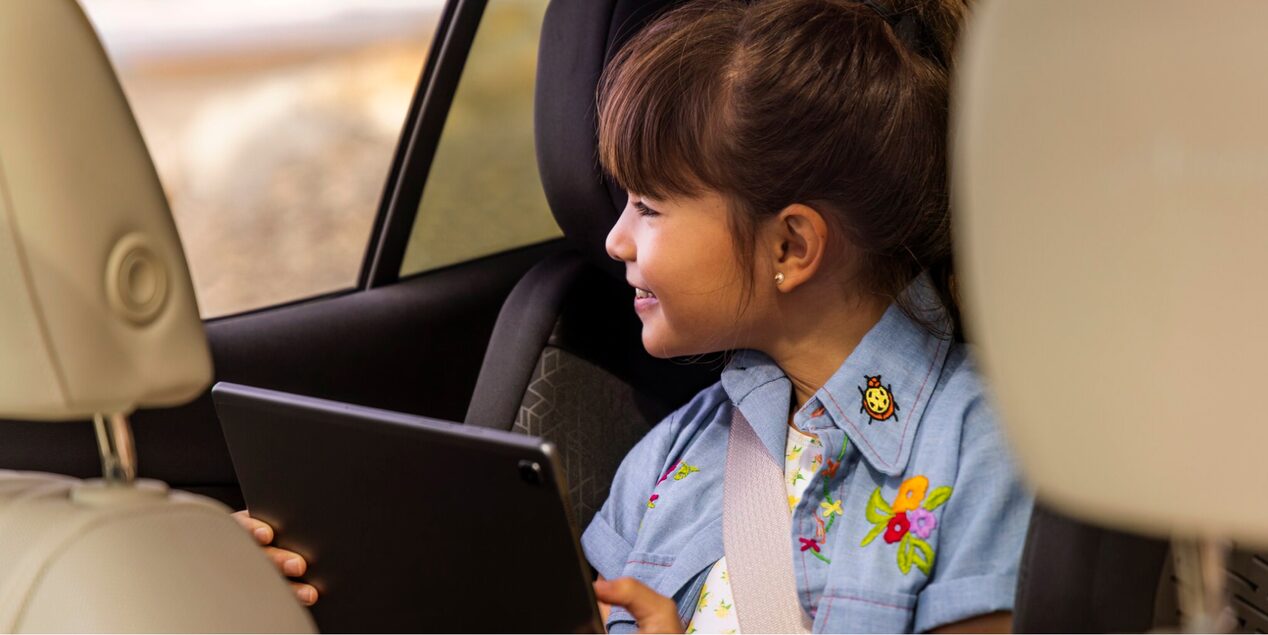 A Young Girl Sitting in her Car Seat Holding an iPad as she Looks out the Car Window