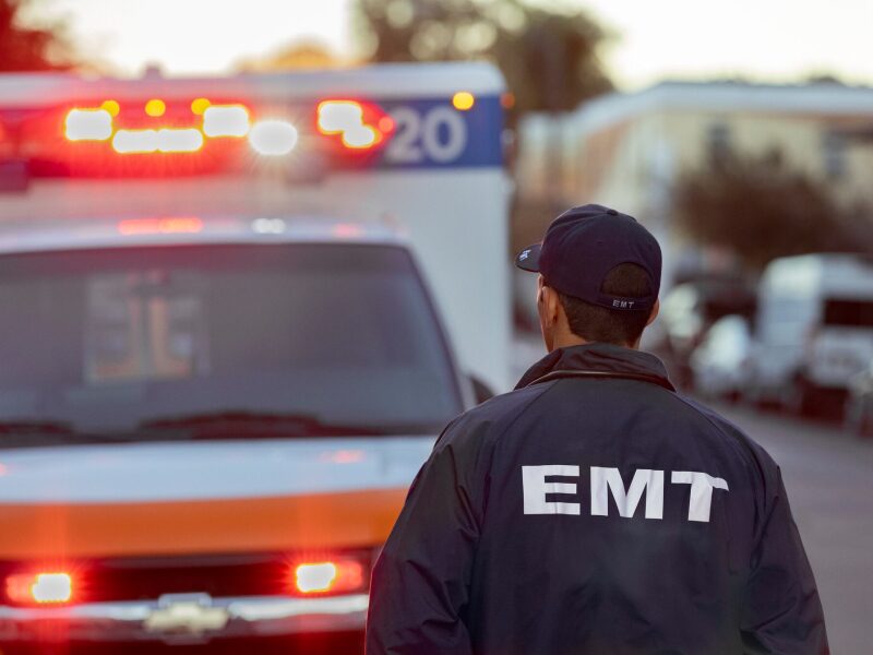An EMT Walking Towards an Ambulance with Their Lights on