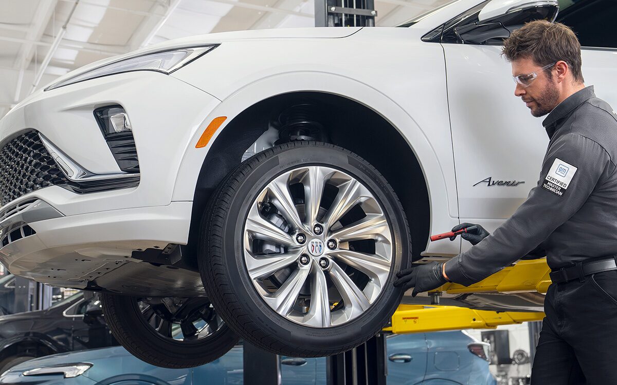 A Male Technician Inspecting a White Vehicle’s Tire While It's Suspended in the Air