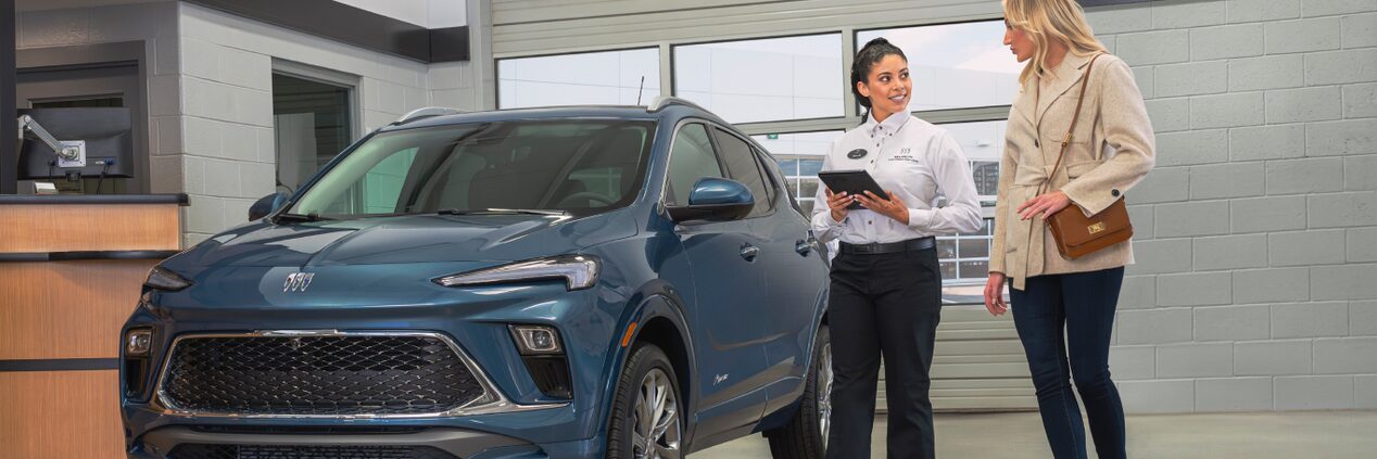 A Buick Certified Service Technician Holding a Tablet Walking with the Customer Next to a Buick Vehicle.