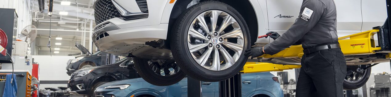 A Male Technician Inspecting a White Vehicle’s Tire While It’s Suspended in the Air