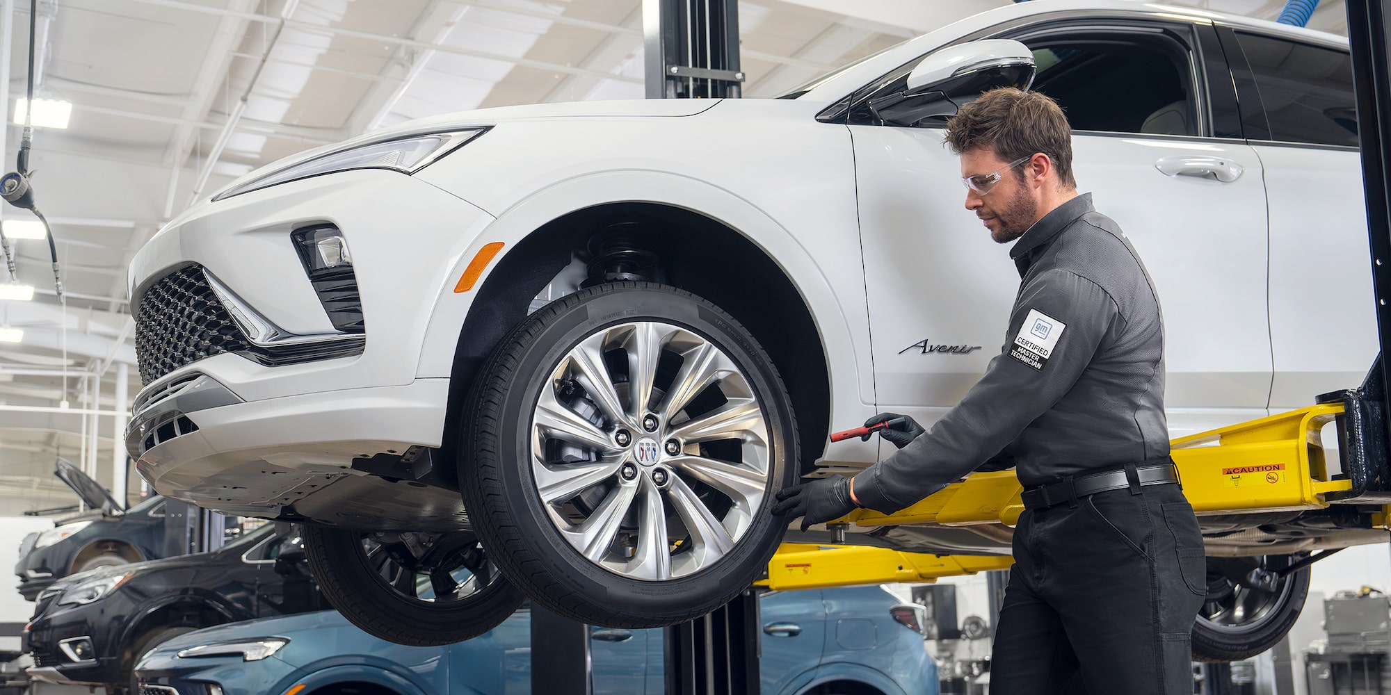 A Male Technician Inspecting a White Vehicle’s Tire While It’s Suspended in the Air