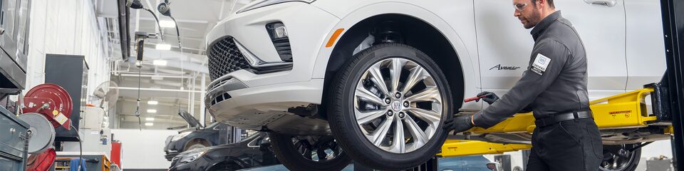 A Male Technician Inspecting a White Vehicle’s Tire While It’s Suspended in the  Air