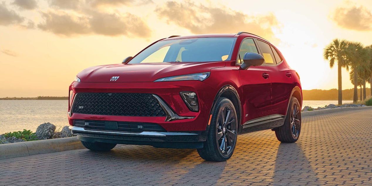 A Red Buick Envista ST Parked on a Patterned Brick Road with a Sunset Sky and Water in the Background