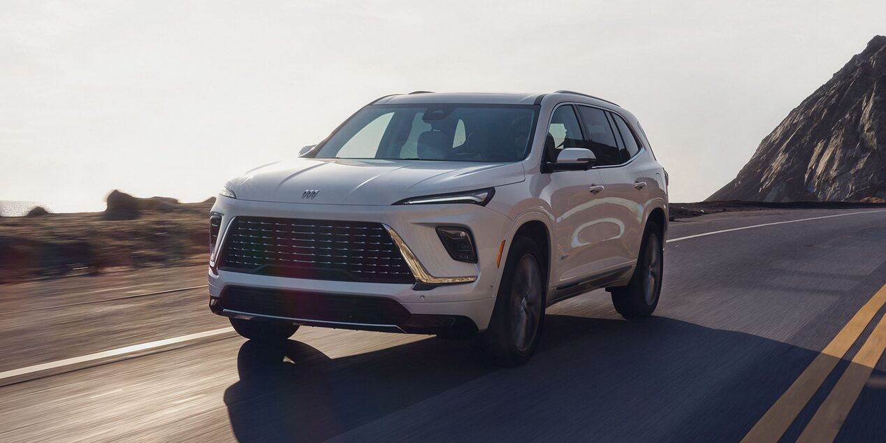Front Three-Quarters View of a White Buick SUV Driving Down a Winding Mountain Road