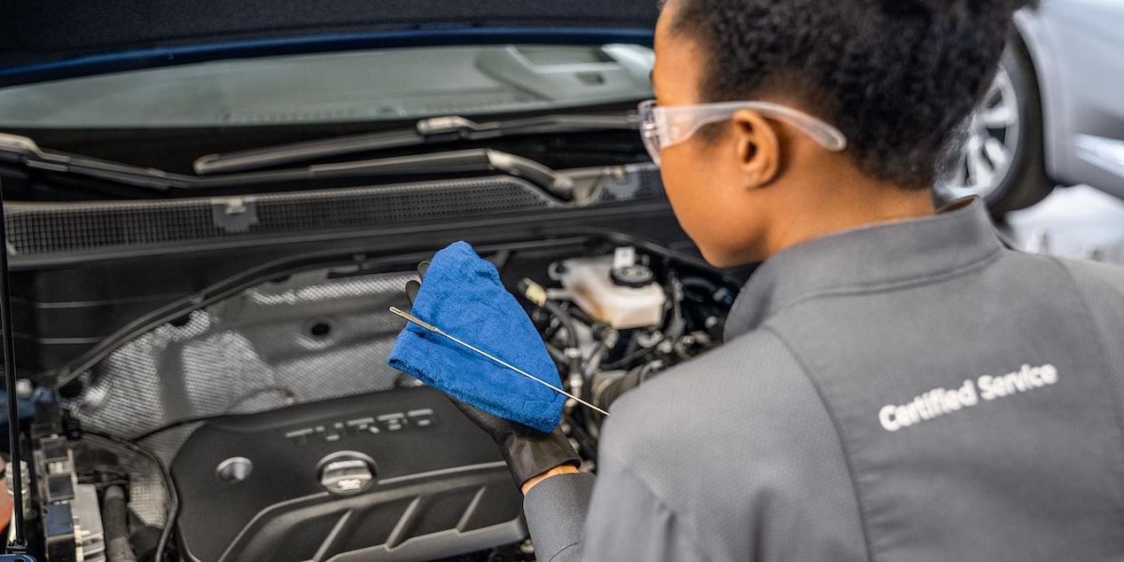 A Technician in Safety Glasses Checks the Oil in a Buick Engine with a Blue Cloth and Dipstick