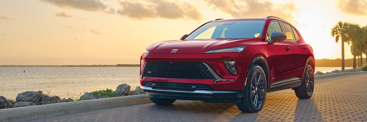 A Red Buick Envista ST Parked on a Patterned Brick Road with a Sunset Sky and Water in the Background