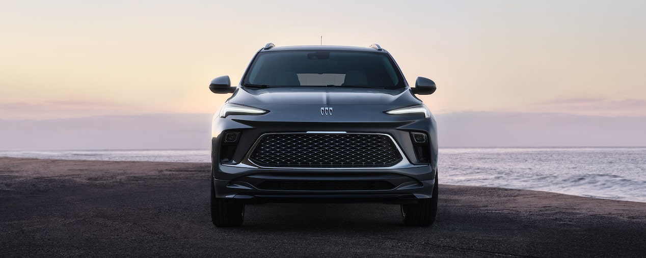 A Dark Gray Buick SUV Parked Facing Forward next to the Ocean During Sunset