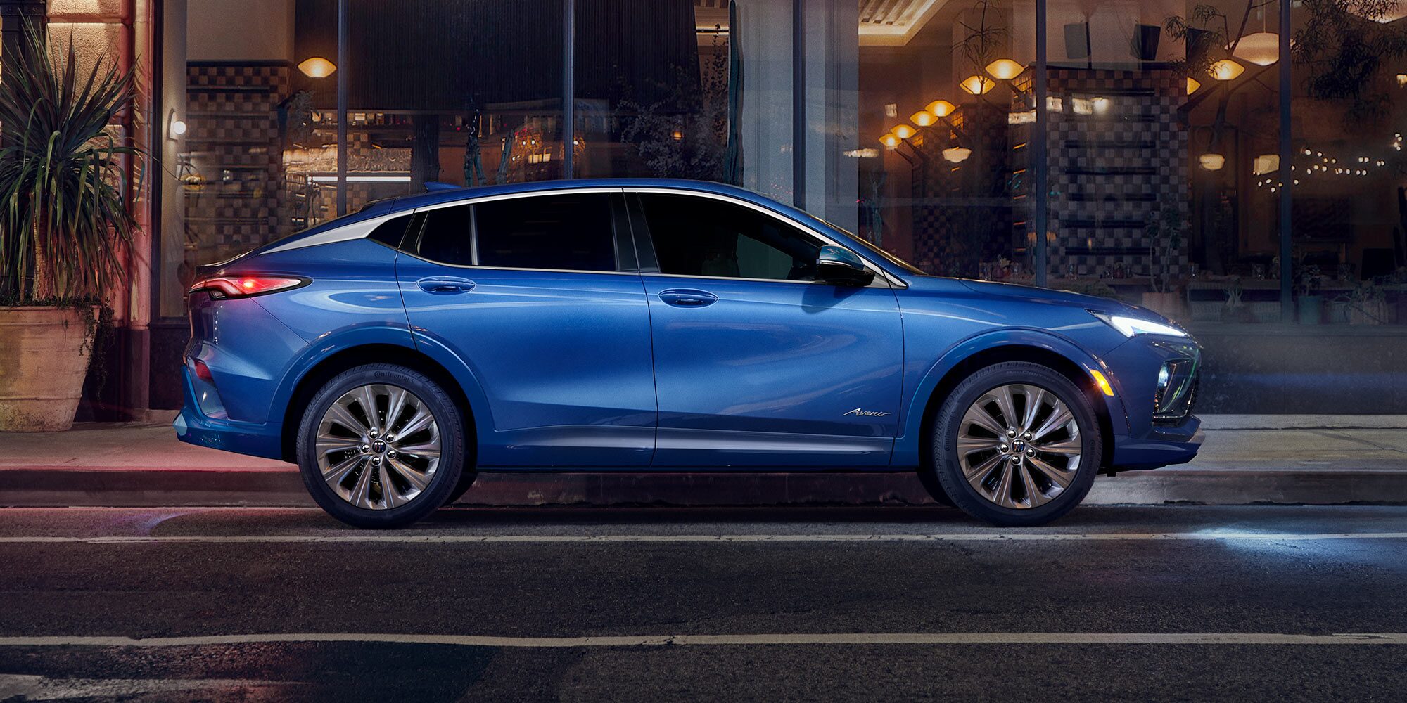 Blue Buick Envista Parked on a City Street at Night with a Lit Building in the Background
