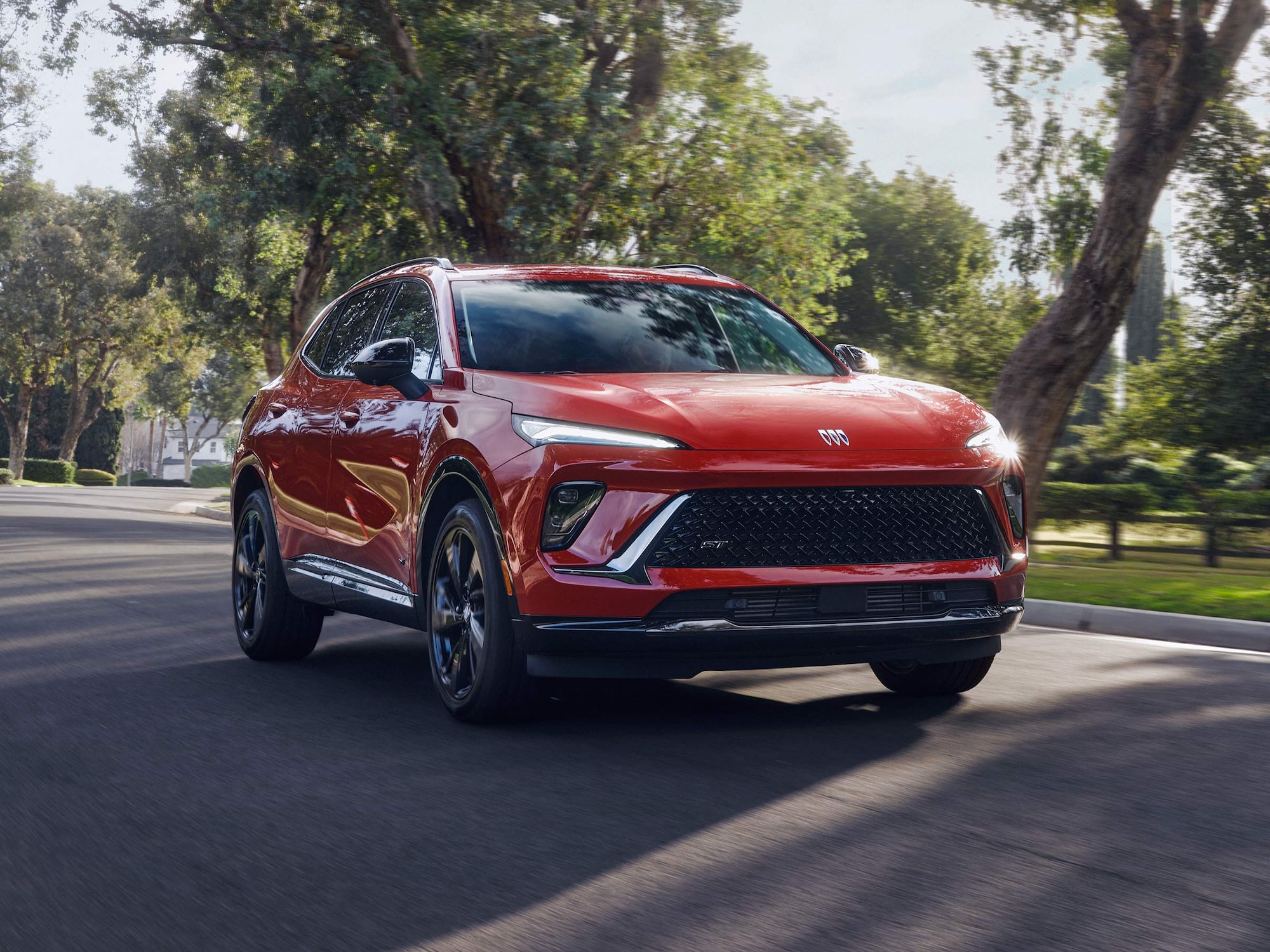 Front Three-Quarters View of a Red Buick SUV Driving Down a Neighborhood Street