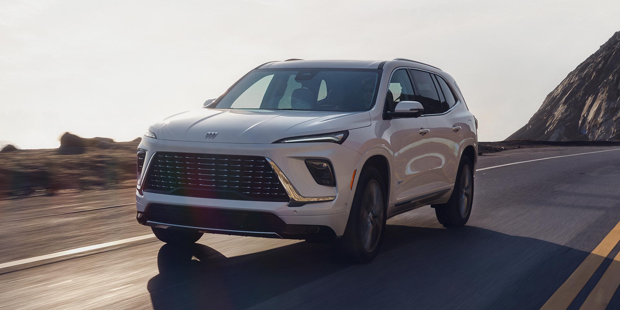 A White Buick SUV Driving Along a Winding Road at Sunset with Mountains in the Background