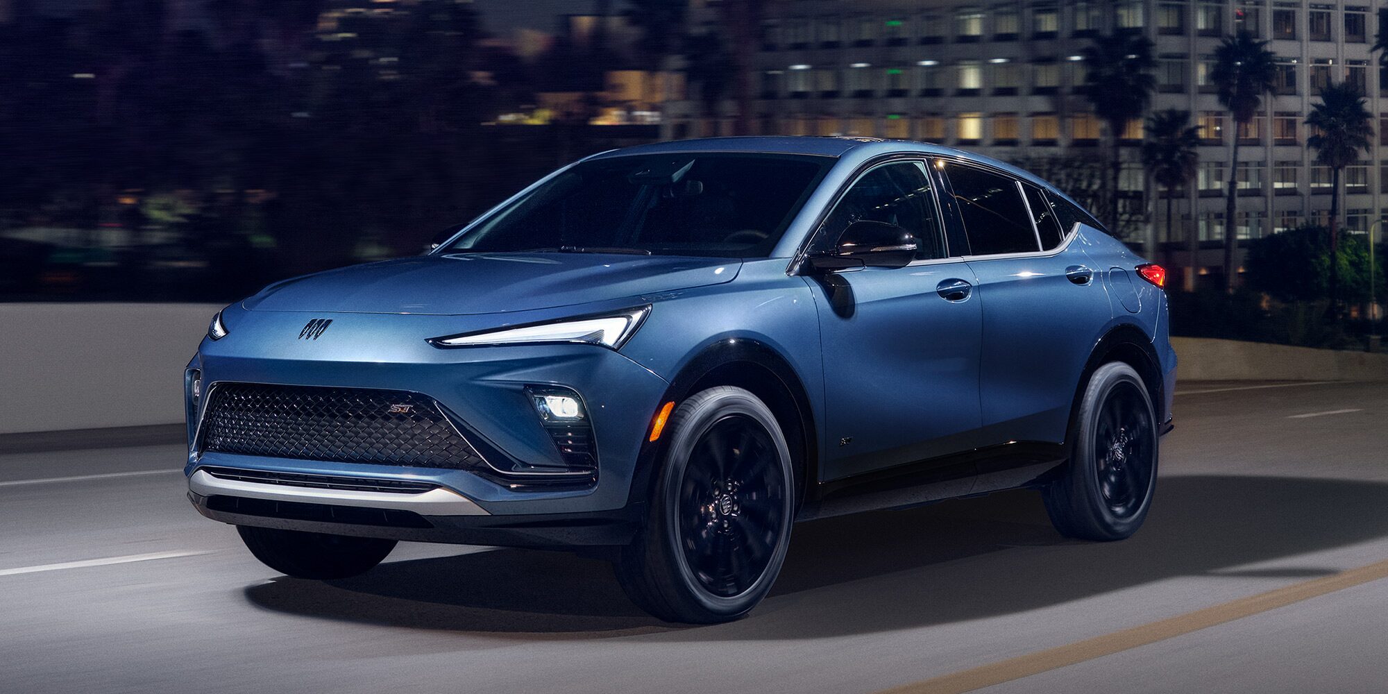 A Blue Buick SUV Driving on a City Street at Night with Illuminated Buildings in the Background