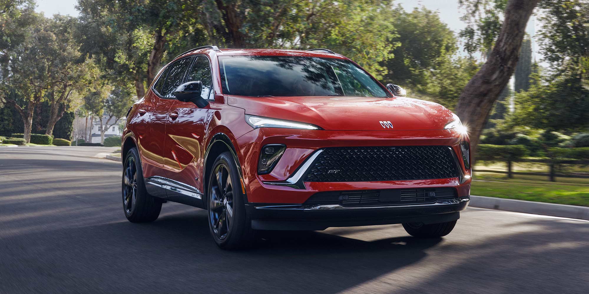 A Red Buick Envista ST Driving Down a Shaded Asphalt Road Lined with Mature Trees