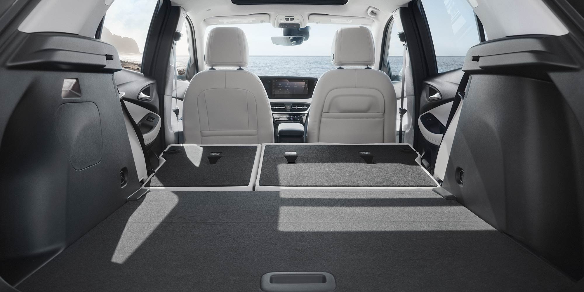 The Interior Cargo Area of a Buick Encore GX SUV with Rear Seats Folded Down Showing Cream Front Seats and a Sunroof with the Ocean in the Background