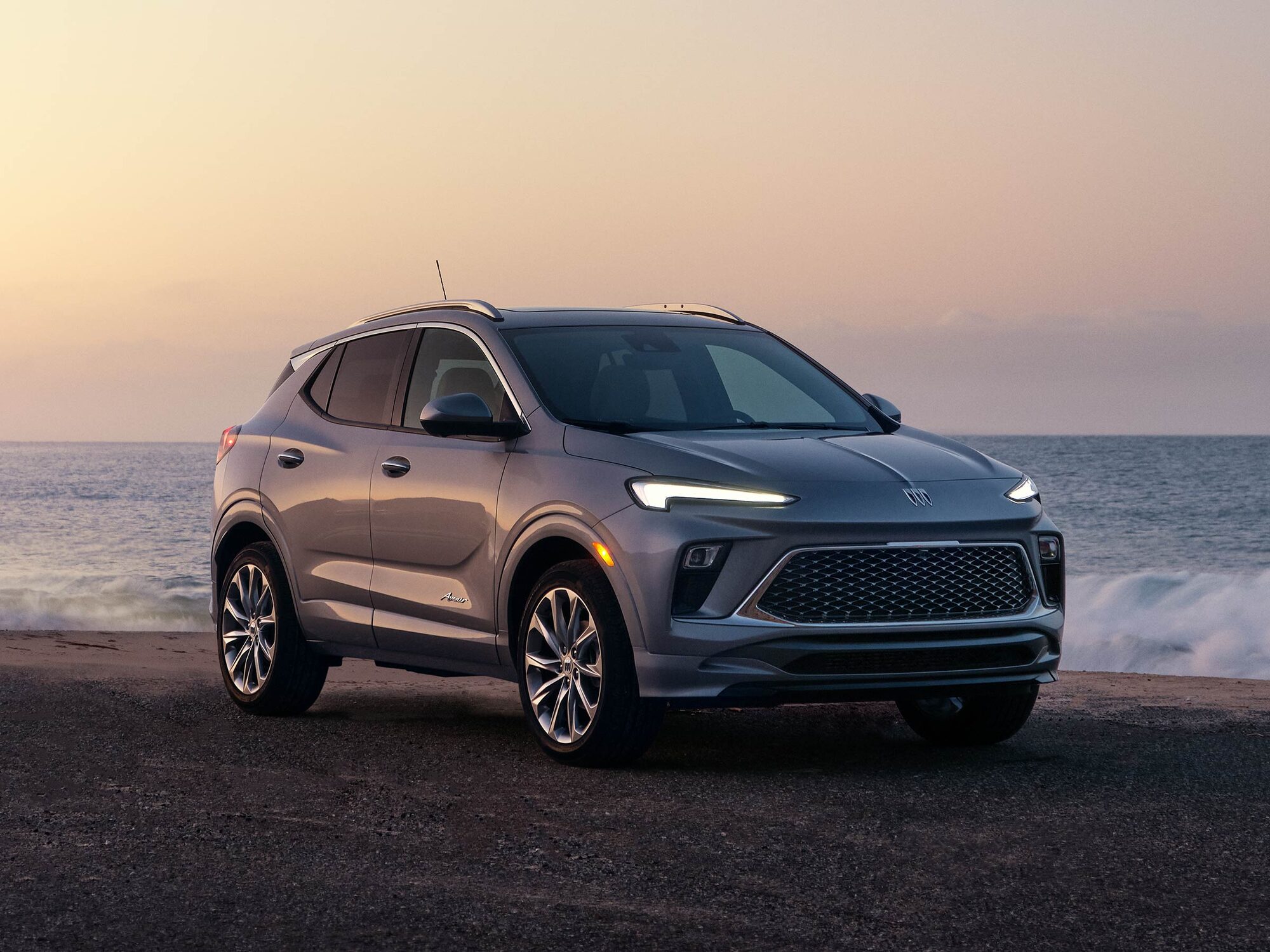 A Gray Buick Encore GX SUV Parked On The Asphalt Road By The Ocean At Sunset