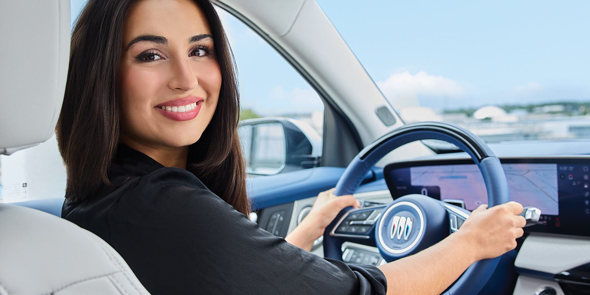 Dalia Elmokadem Smiles While Driving a Buick Vehicle, Holding the Blue Steering Wheel with the Buick Logo Prominently Displayed