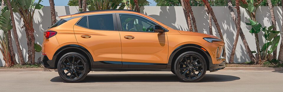 Side View of an Orange Buick SUV with the Backdrop of a Wall with Trees