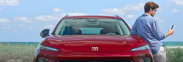 Man in Blue Shirt Leaning on Red Buick Car and Looking at His Phone