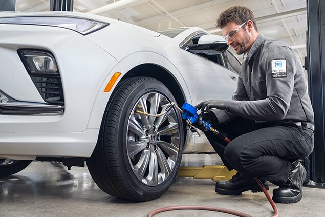 Male Technician Bending Down Working on the Tire of White Vehicle